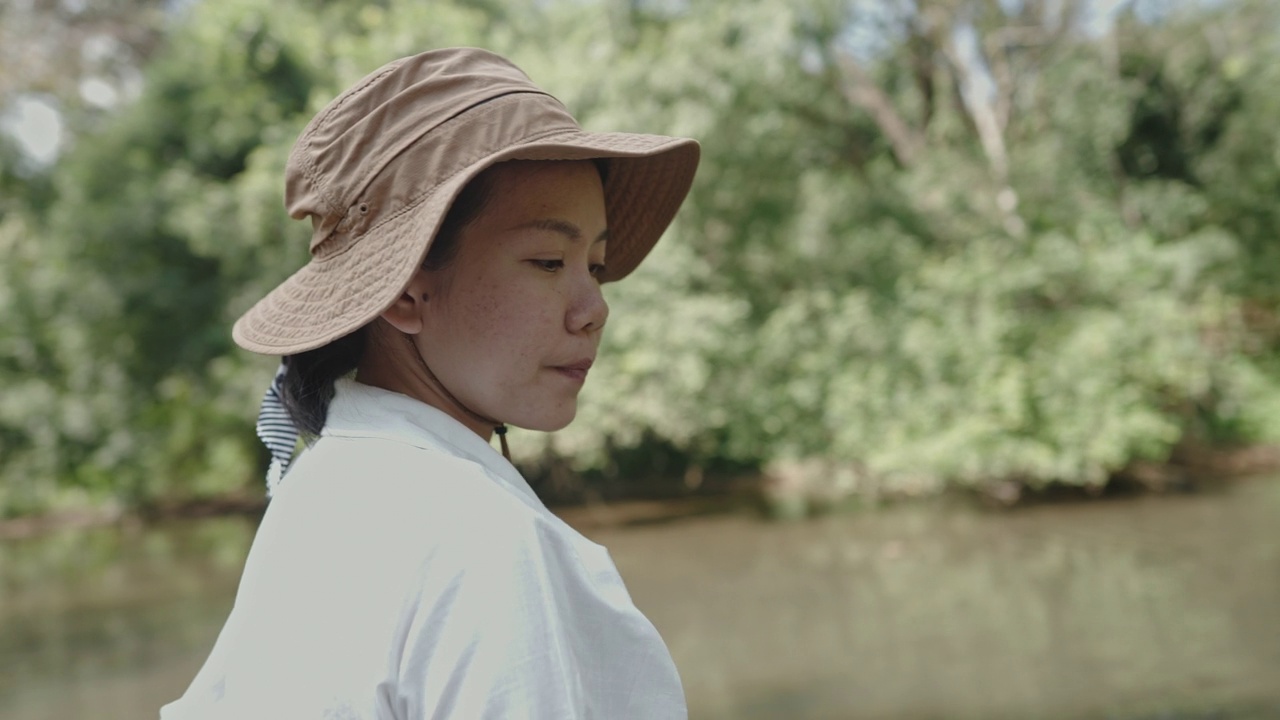 中景拍摄的是一名年轻女子在森林里的小溪流边休闲享受视频素材