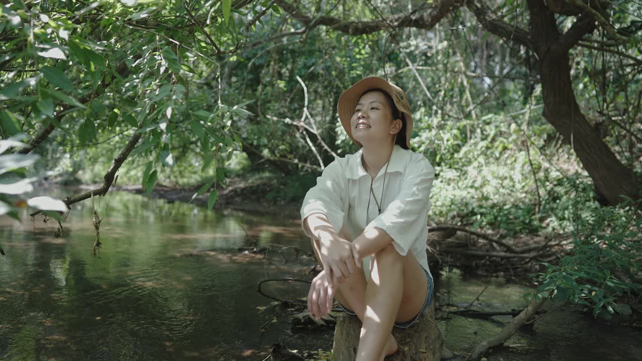 中景拍摄的是年轻成年女子在森林小溪边的休闲享受视频素材