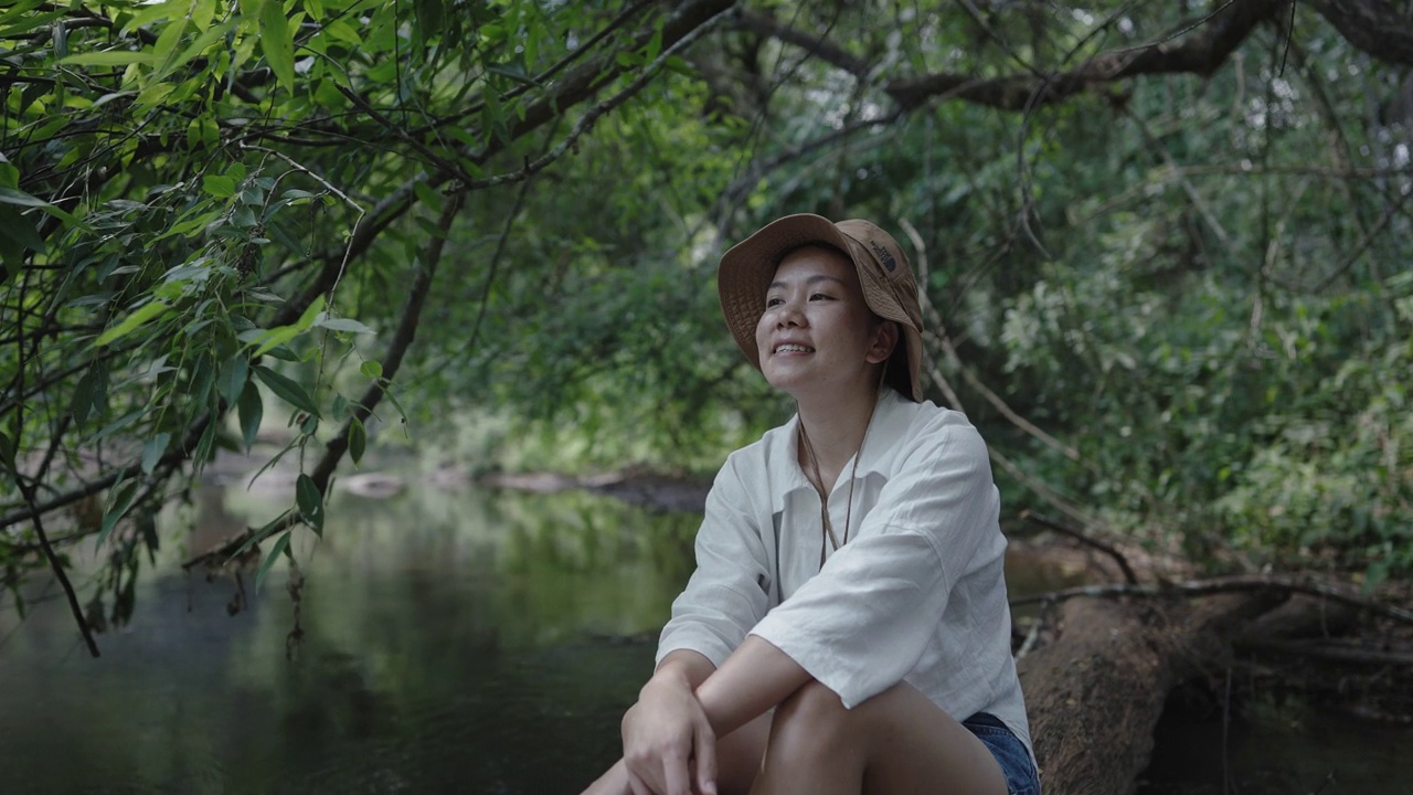 中景拍摄的是一名年轻女子在森林里的小溪流边休闲享受视频素材