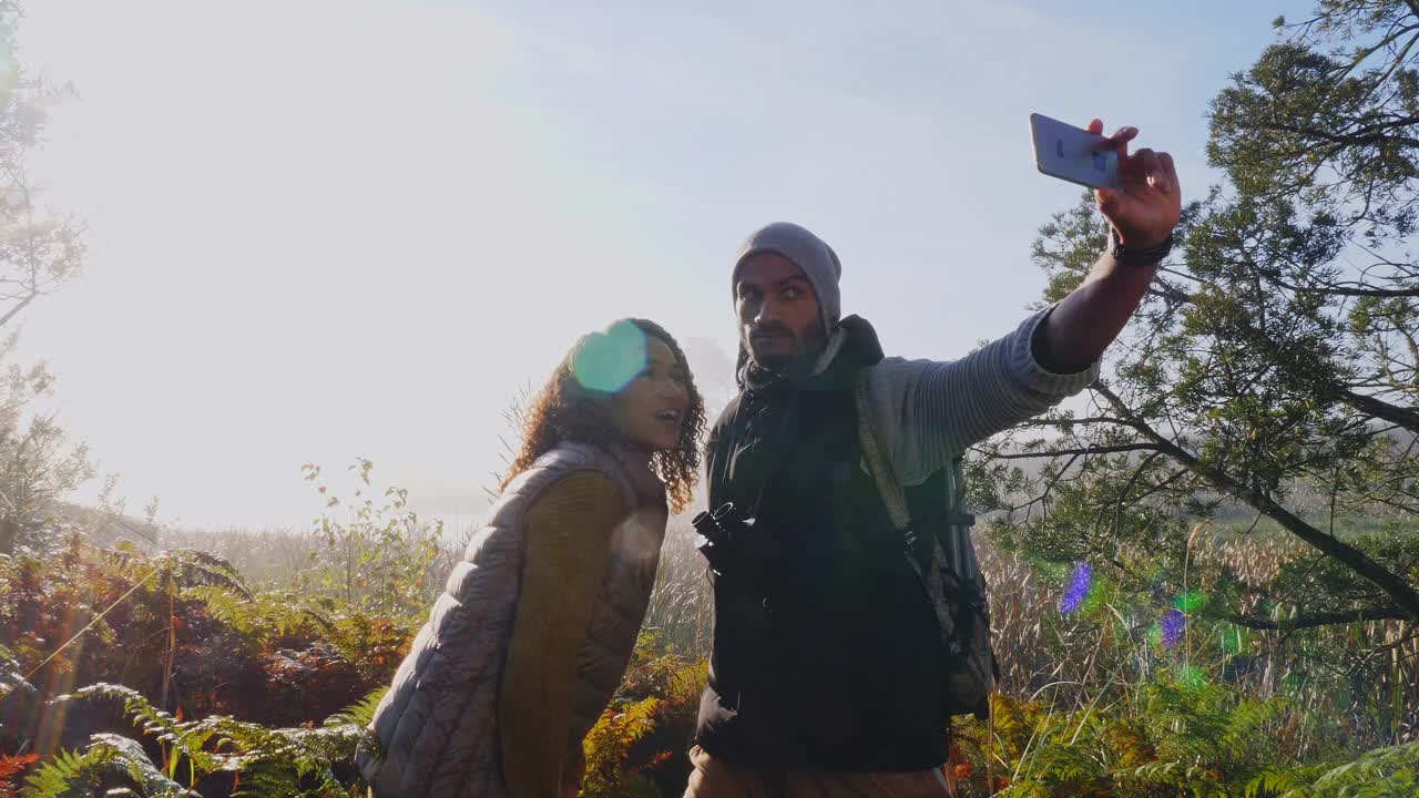 好玩的年轻徒步旅行者夫妇在阳光明媚的秋天树林里自拍视频素材