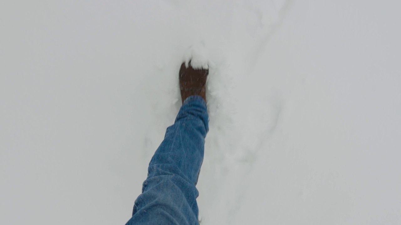 男性腿的俯视图。一个男人穿着时尚的靴子走在白雪覆盖的人行道上视频素材