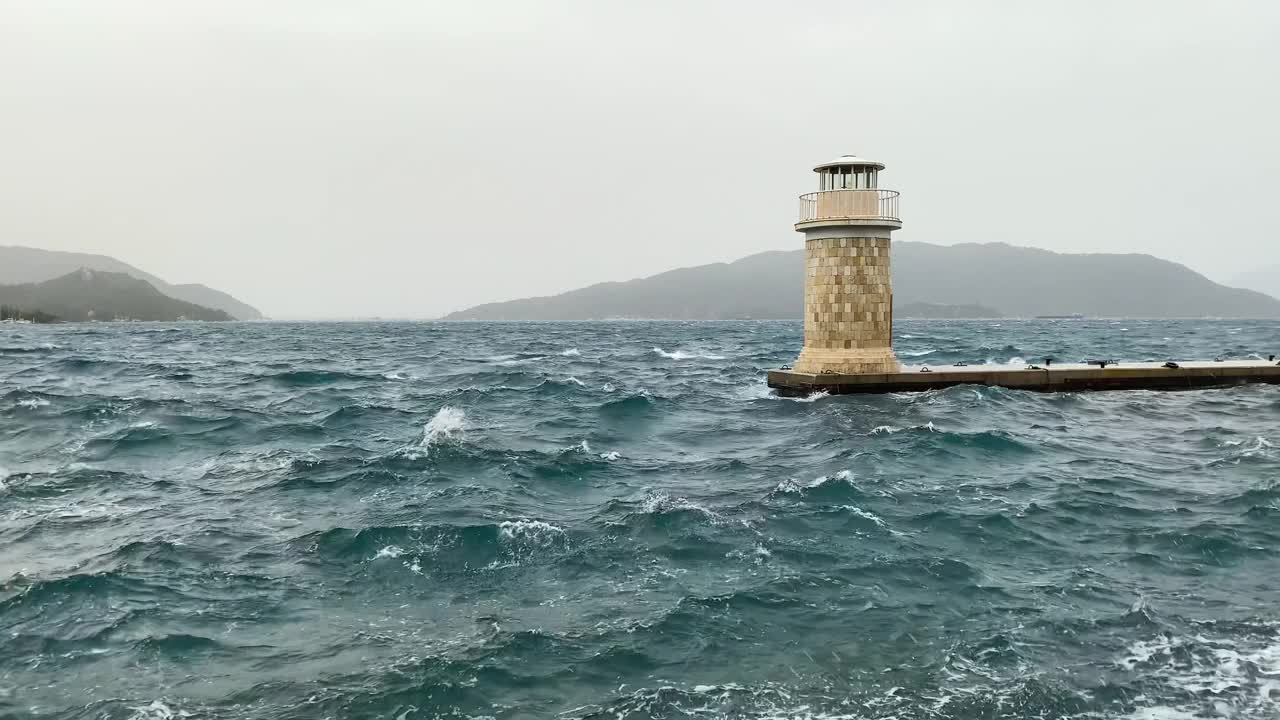 海浪拍打在带有小防波堤和灯塔的城市堤岸上。暴风雨天气。视频素材