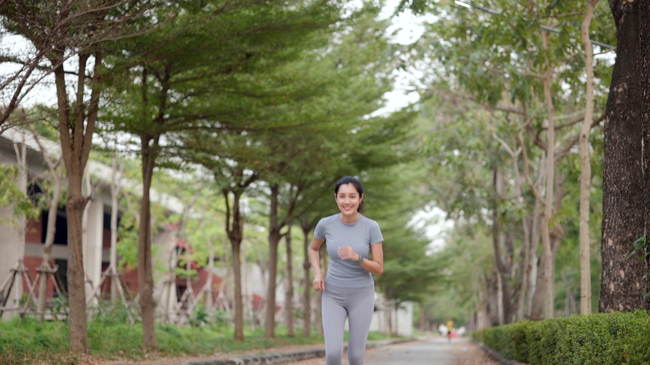 快乐苗条的女人穿着运动服在日出的城市慢跑。年轻美丽的亚洲女性在运动胸罩跑步户外。早上做运动。健康积极的生活方式理念。视频素材