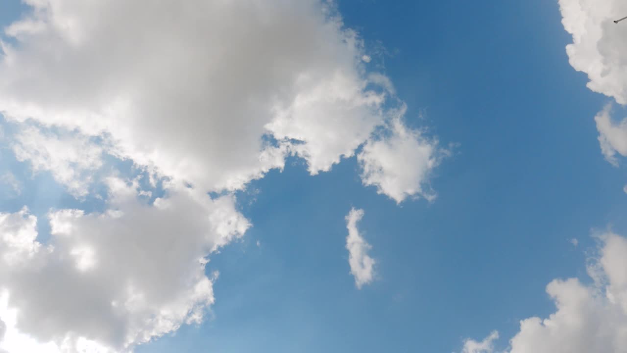 4K时间推移广角镜头仰望阳光，在蓝天上投射出一团蓬松的白云。云和天空的自然背景视频素材