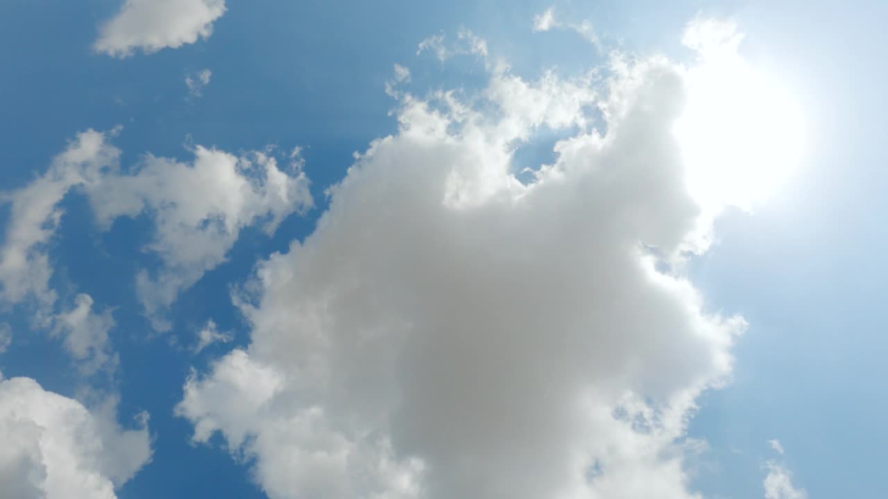 4K时间推移广角镜头，看着太阳在蓝色的天空闪耀着蓬松的白云。云和天空的自然背景视频素材