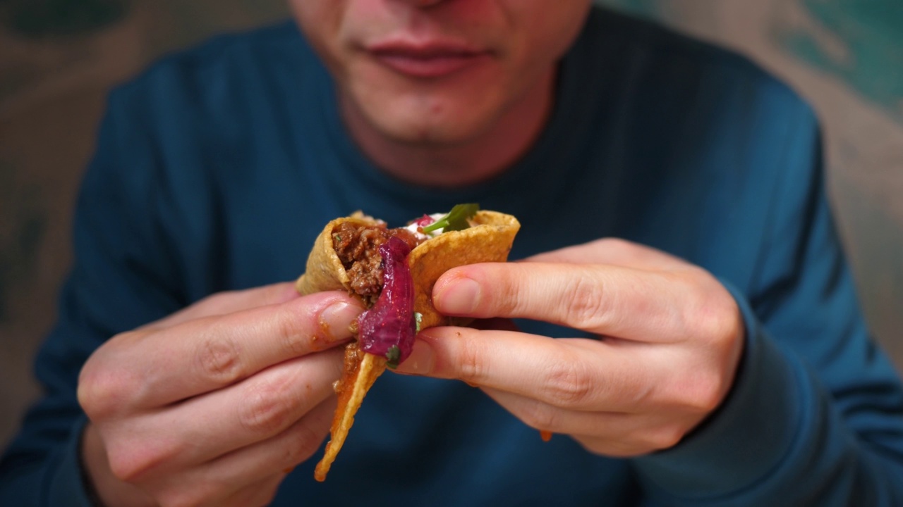 在墨西哥美食餐厅里，一个穿着蓝色毛衣的男人正在吃美味多汁的墨西哥卷饼视频素材