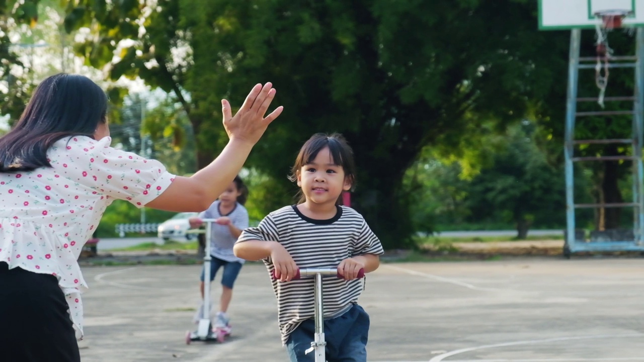 快乐的妈妈和孩子们在夏天的公园里骑着滑板车击掌。在户外玩滑板车的孩子们。儿童休闲活动和户外运动视频素材