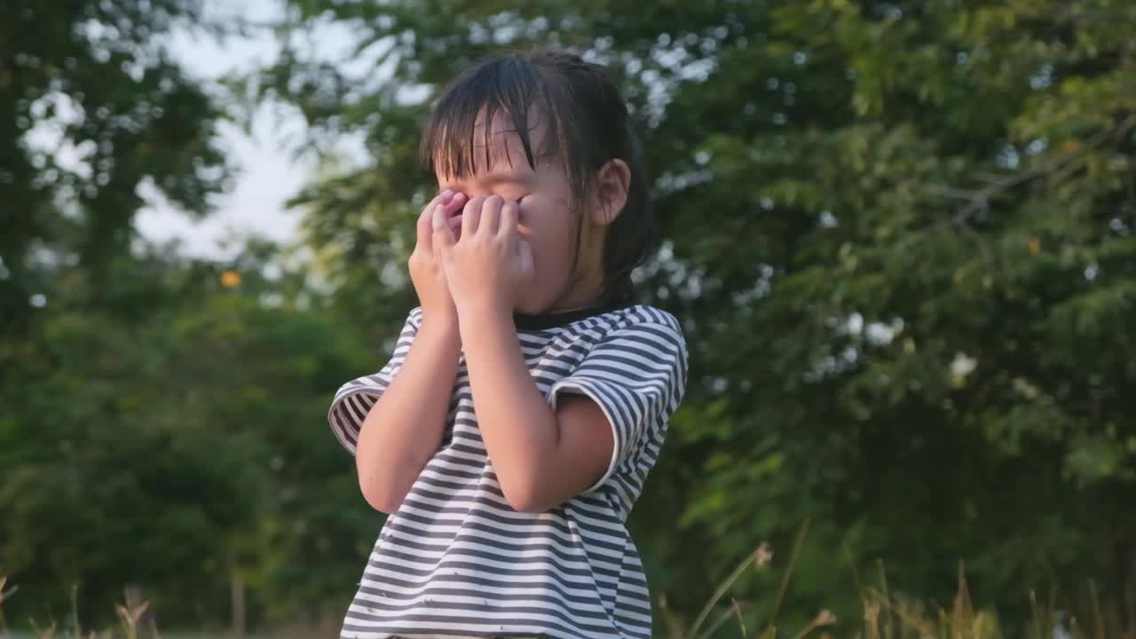 快乐的亚洲小女孩捂着眼睛在公园里玩捉迷藏。快乐的家庭在假期一起做活动。视频素材