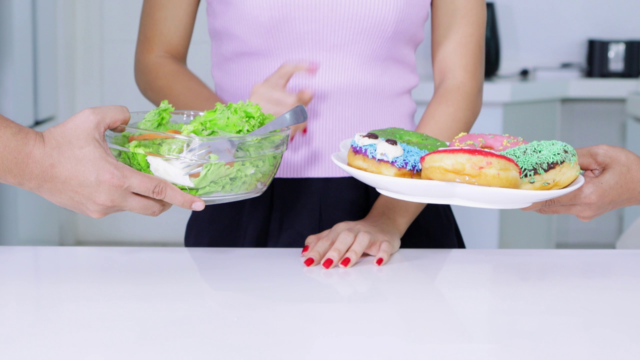 节食的概念。一个陌生女人用手势选择了一盘甜甜圈，拒绝了一碗沙拉。拍摄分辨率为4k视频素材