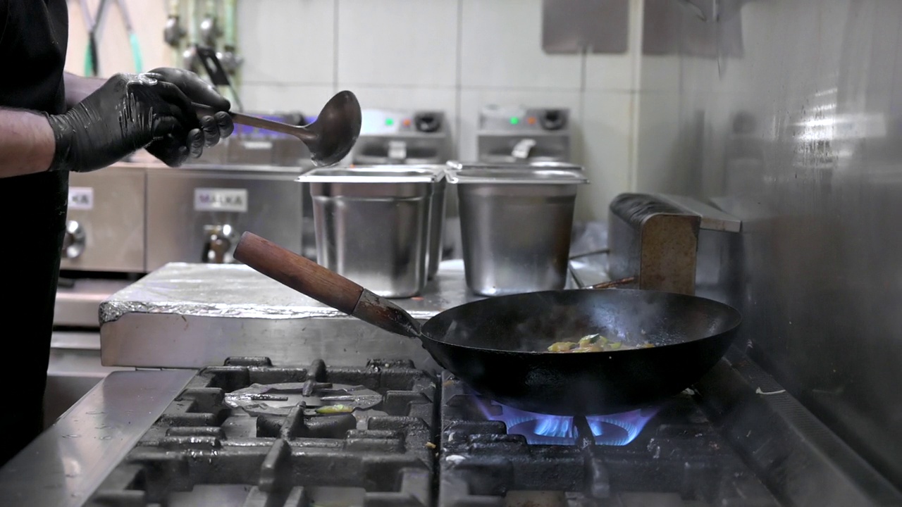 厨师在厨房煮锅的慢镜头。餐厅炒锅火烹饪近距离，在商业厨房煮炒蔬菜。高质量的FullHD镜头视频素材