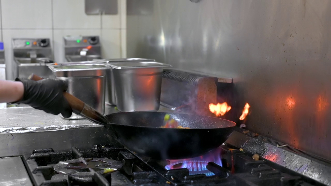 厨师在厨房煮锅的慢镜头。餐厅炒锅火烹饪近距离，在商业厨房煮炒蔬菜。高质量的FullHD镜头视频素材