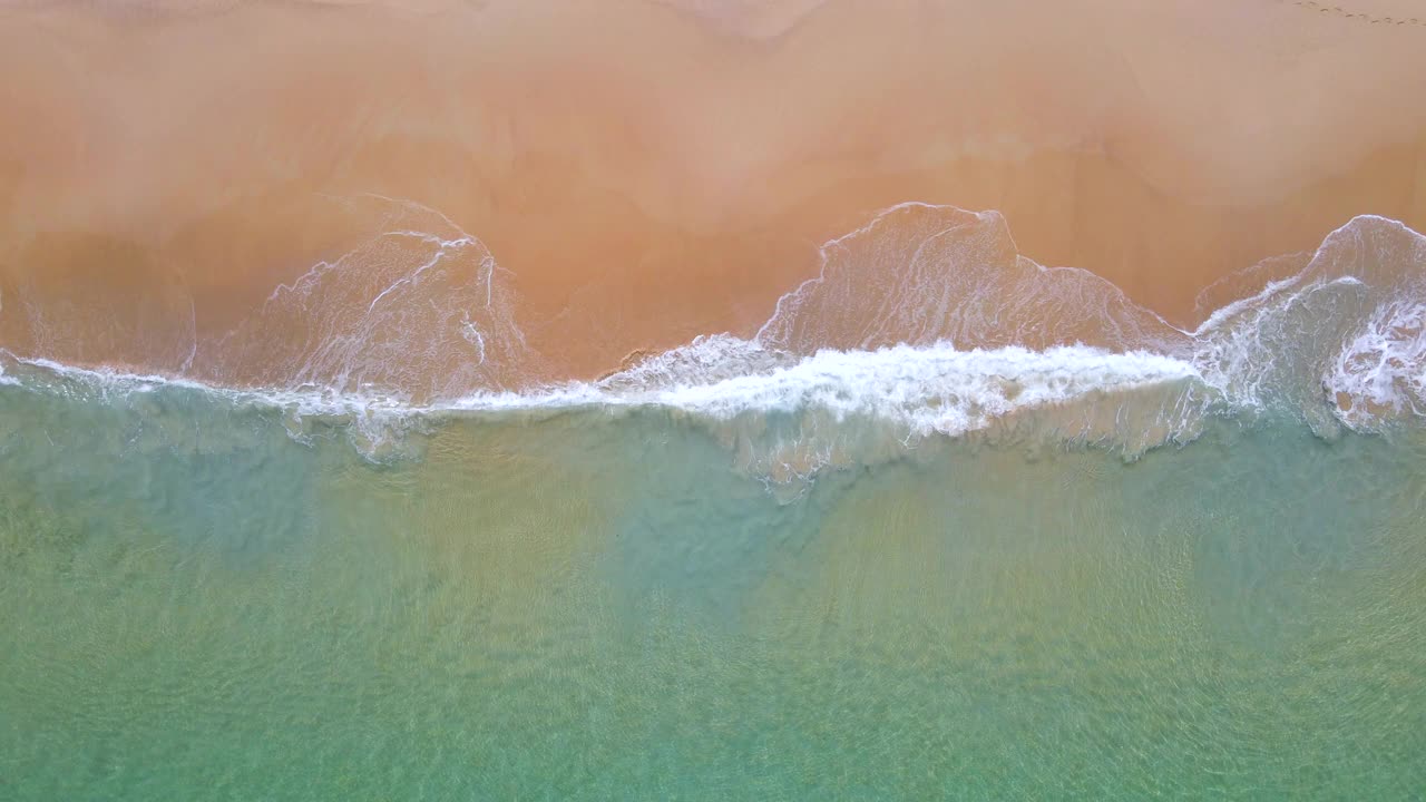 蓝绿色的海浪到达海岸线的鸟瞰图。从顶部俯瞰美丽的热带海滩景观。泰国安达曼海。视频素材