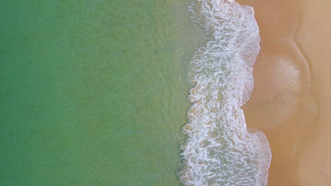 蓝绿色的海浪到达海岸线的鸟瞰图。从顶部俯瞰美丽的热带海滩景观。泰国安达曼海。视频素材