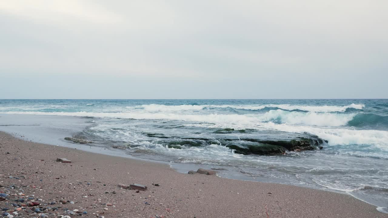 小波浪卷着云朵涌向岩石海滩。有海浪的石滩。岩石海滩上的日落。海浪撞击岩石视频素材