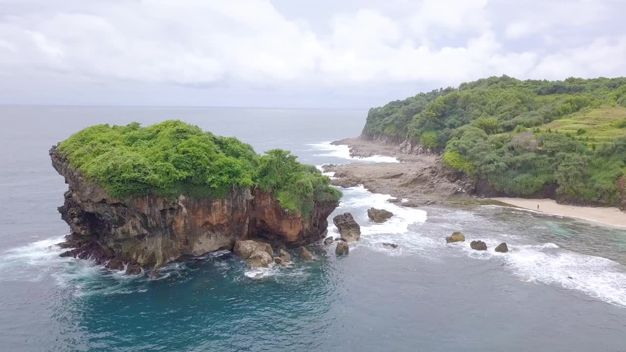 无人机拍摄的珊瑚岛被绿树覆盖，被热带海滩的海浪拍打着。视频素材