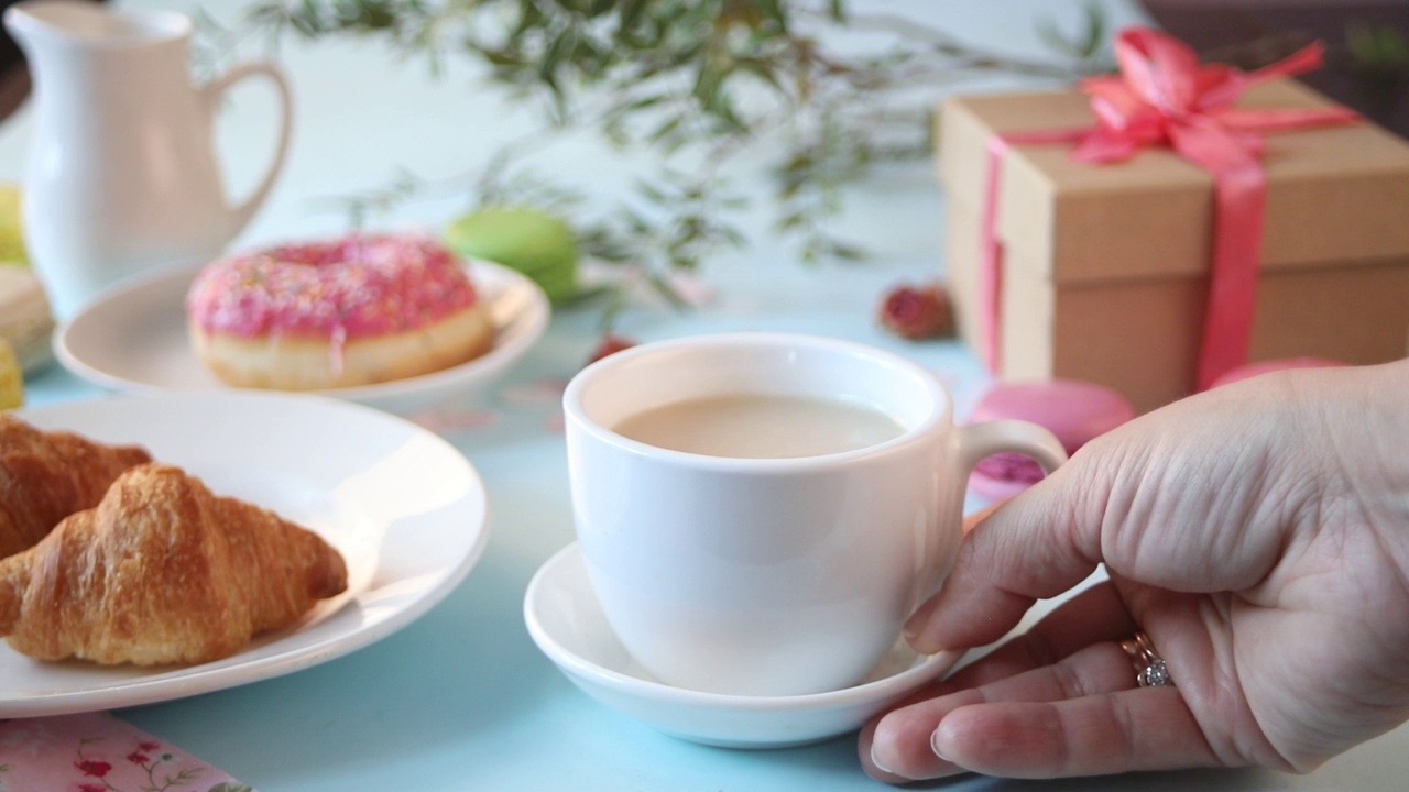 女人手把茶杯放在桌子上。背景是新鲜出炉的牛角面包。健康早餐生活理念视频下载