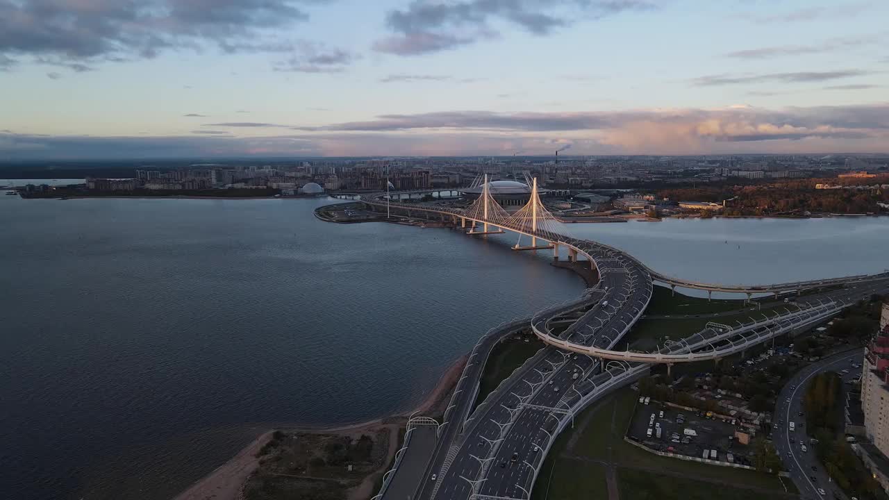 航拍的弯曲的多车道公路横跨涅瓦河。许多汽车在路上快速行驶。城市景观，塔桥和泽尼特体育场的背景。视频素材