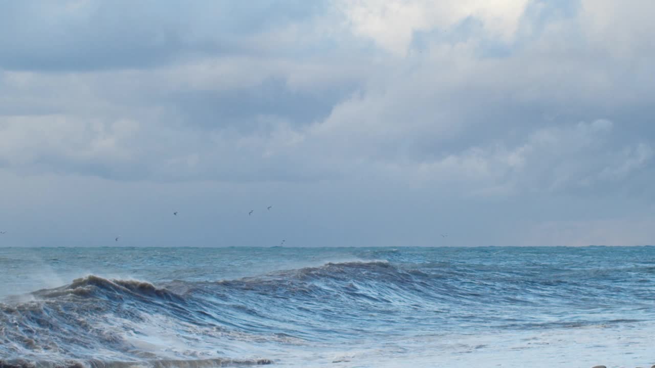 巨大的海浪拍打着海岸，蓝色的海水背景。海面上的风暴和汹涌的海浪溅起泡沫。刮风坏天气慢动作视频素材