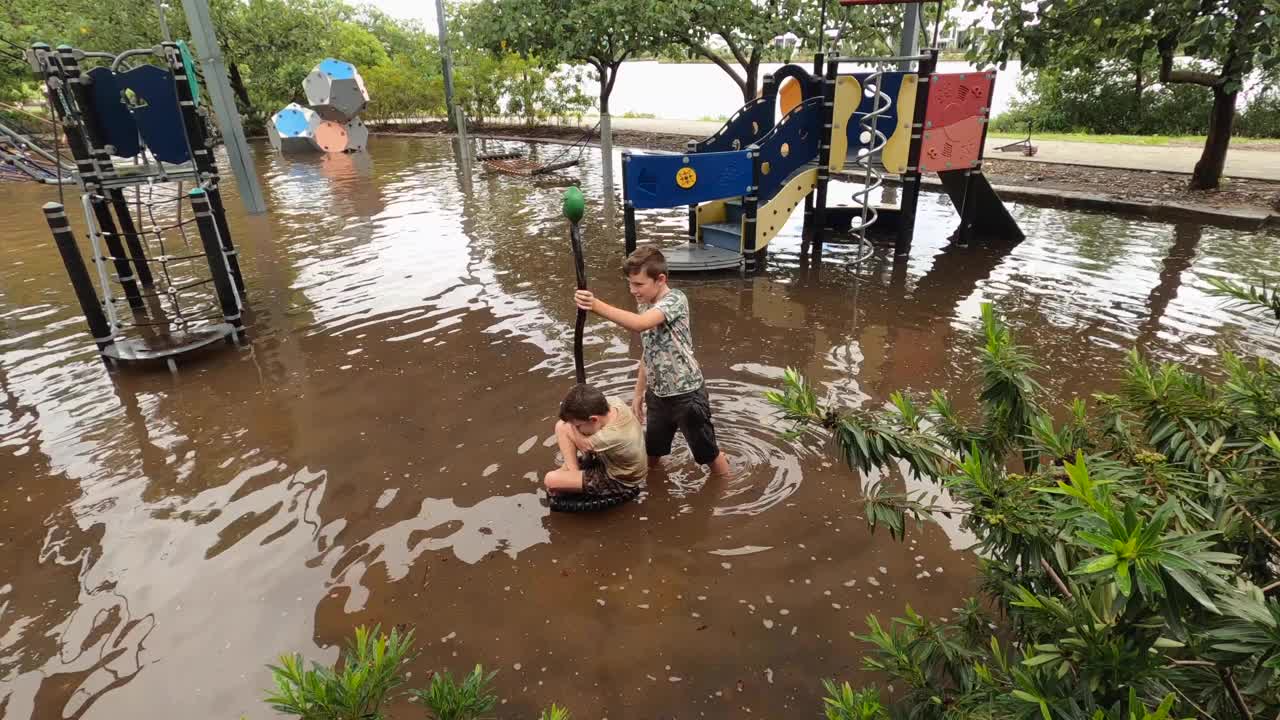 两个快乐的小男孩在湿漉漉的操场上玩旋转游戏设备。视频素材