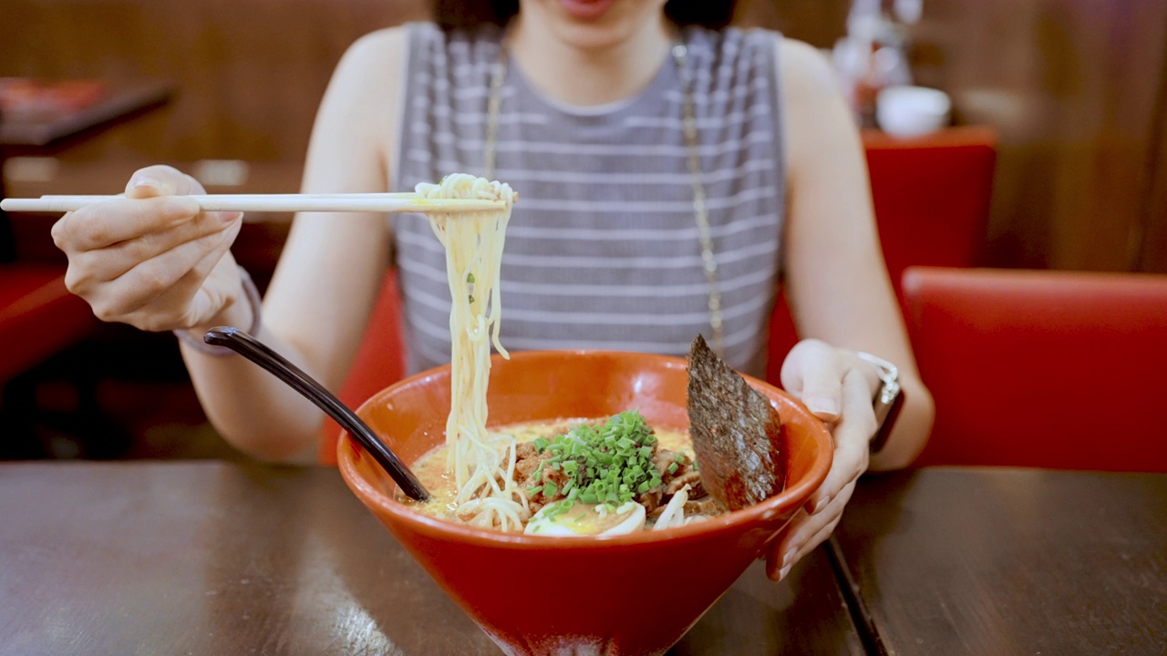 年轻女子在餐厅的木桌上吃着一碗辣味噌拉面视频素材