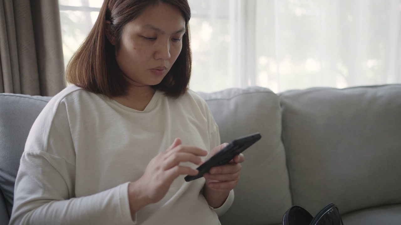 女人在沙发上放松，在家里玩手机视频素材