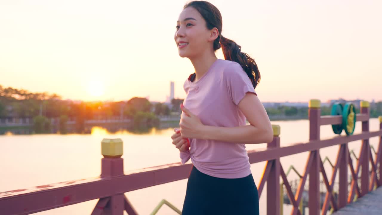 亚洲年轻美丽的运动女子在公园的街道上跑步。美丽的运动员和坚定的女孩在运动服装锻炼慢跑锻炼户外保健在傍晚日落在花园。视频素材