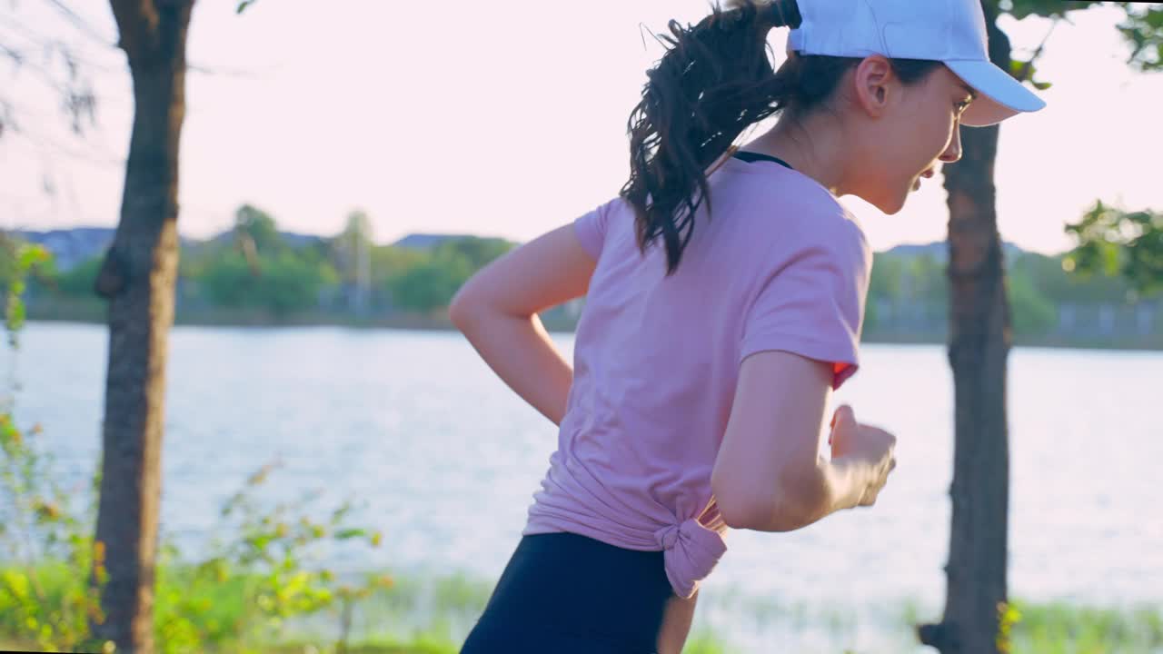 亚洲年轻美丽的运动女子在公园的街道上跑步。美丽的运动员和坚定的女孩在运动服装锻炼慢跑锻炼户外保健在傍晚日落在花园。视频素材