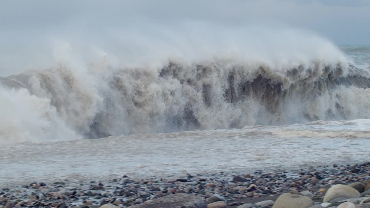 巨大的海浪拍打着海岸，蓝色的海水背景。海面上的风暴和汹涌的海浪溅起泡沫。刮风坏天气慢动作视频素材