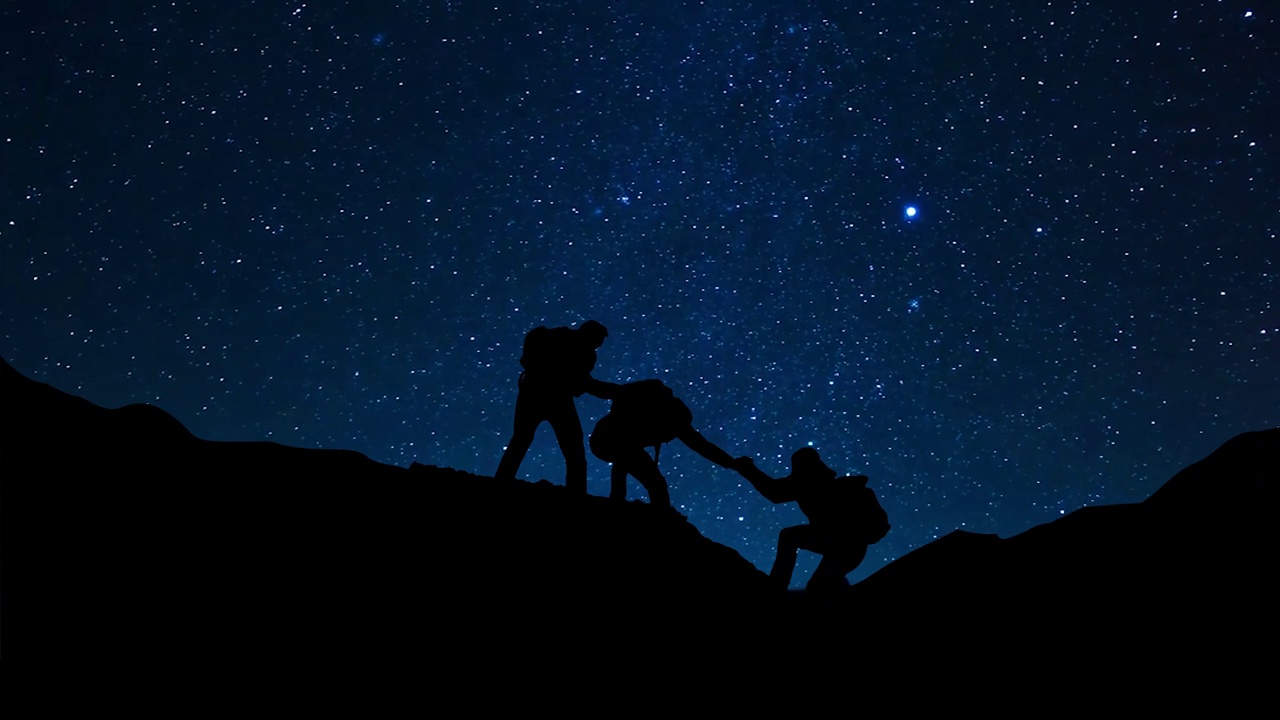 一个男人的剪影，在星夜帮助队员攀登。视频素材