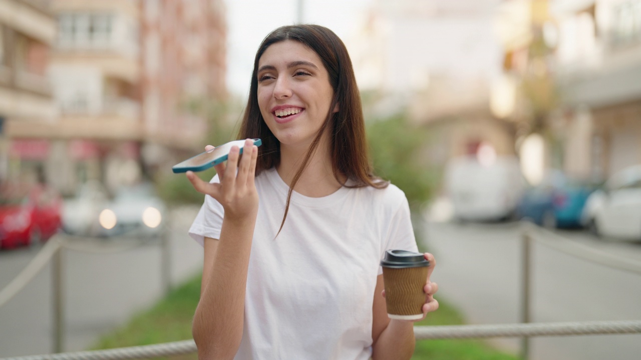 年轻的西班牙女孩在街上边喝咖啡边用智能手机聊天视频素材