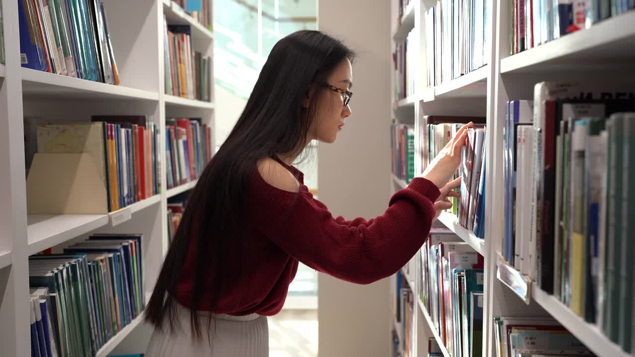 日本女学生在大学图书馆寻找书籍，挑选小说或课程作业材料视频素材