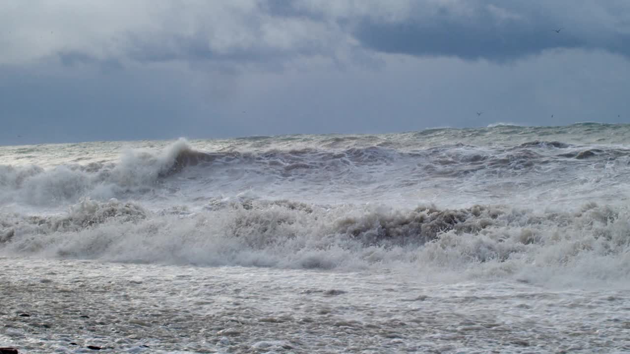 巨大的海浪拍打着海岸，蓝色的海水背景。海面上的风暴和汹涌的海浪溅起泡沫。刮风坏天气慢动作视频素材