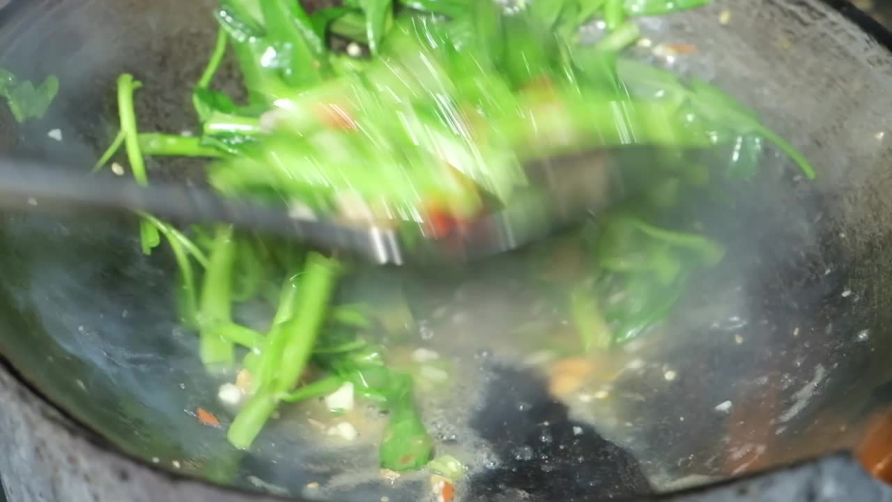 近距离烹饪泰国风味的食物，美味的炒牵牛花与酥脆的猪肉在热煎锅在厨房泰国餐厅。视频素材