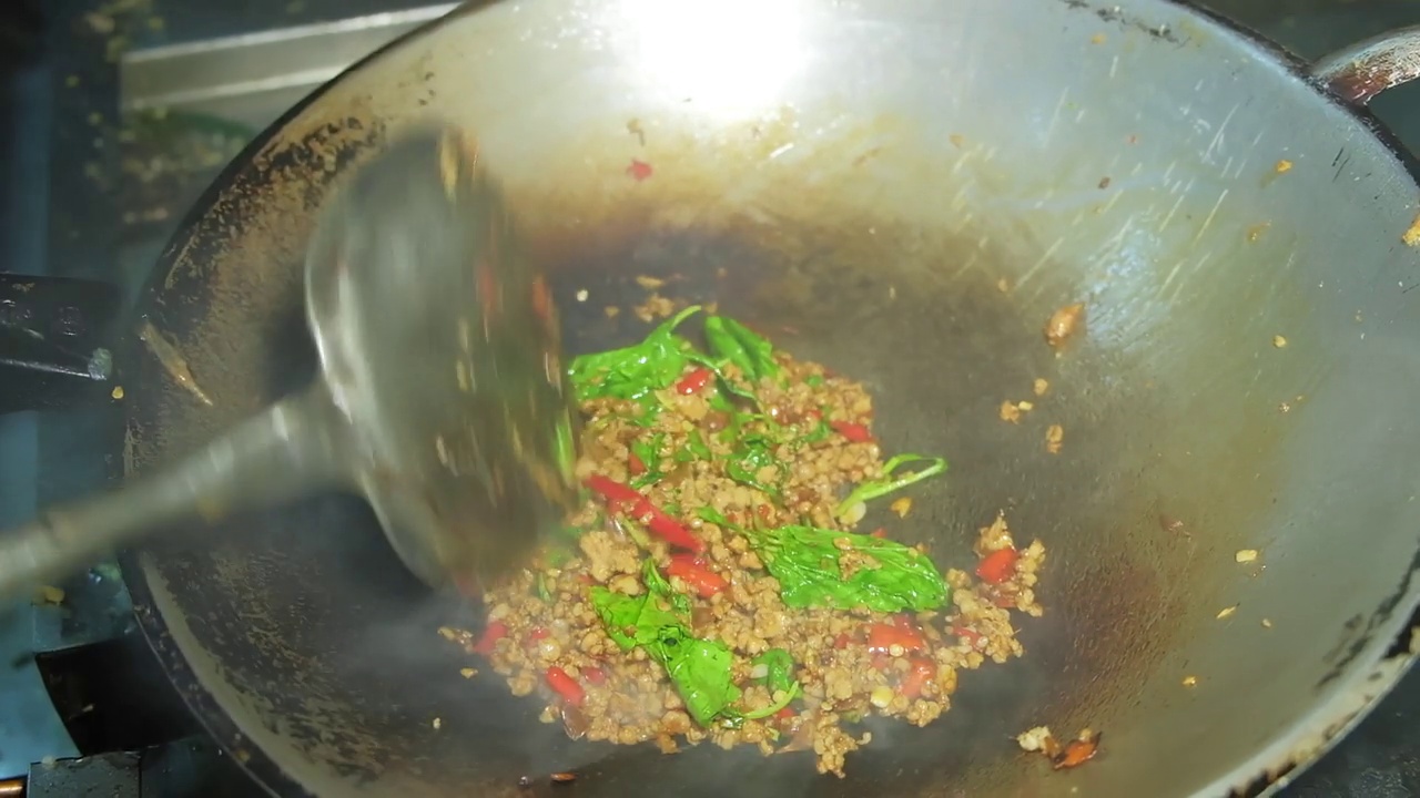 近距离烹饪泰国传统的受欢迎的食物在泰国餐馆的煎锅里用罗勒叶炒碎猪肉视频素材