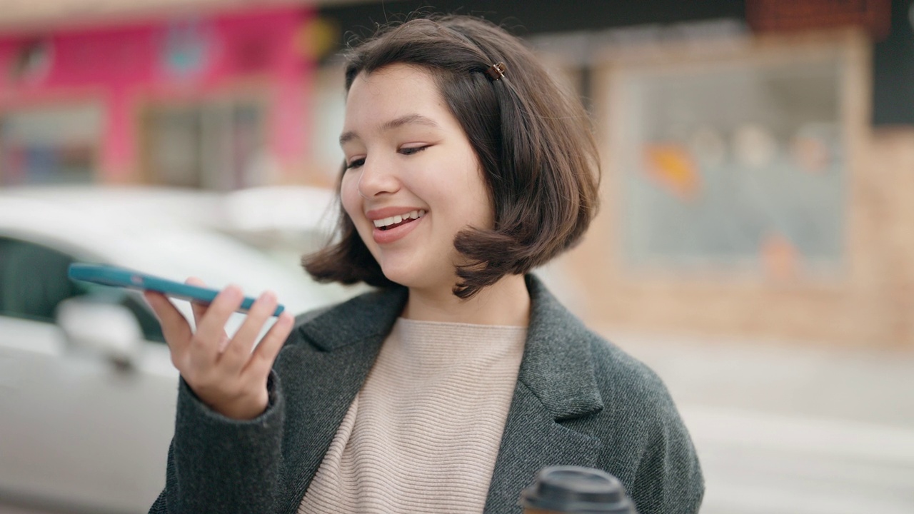 年轻的西班牙女孩在街上边喝咖啡边用智能手机聊天视频素材