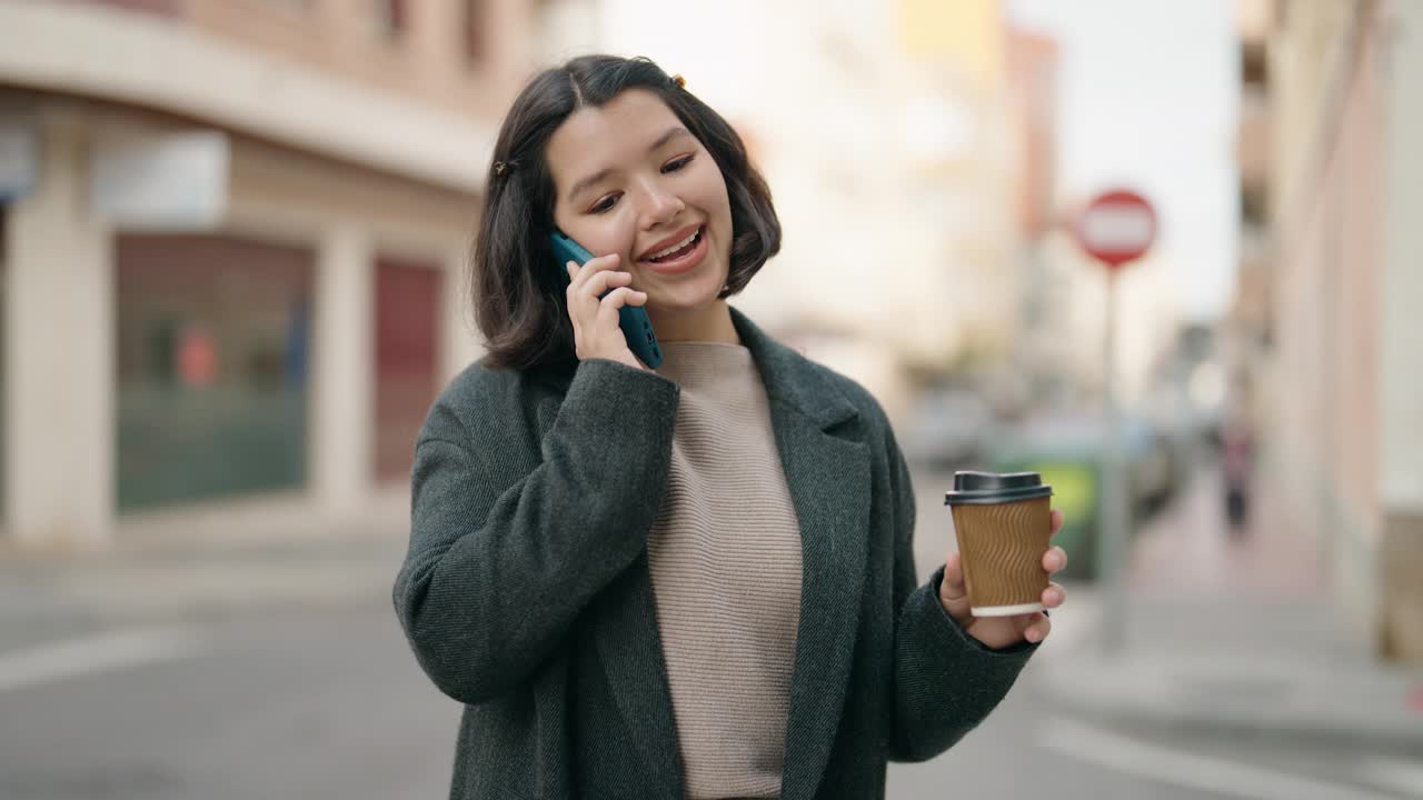 年轻的西班牙女孩在街上边喝咖啡边用智能手机聊天视频素材