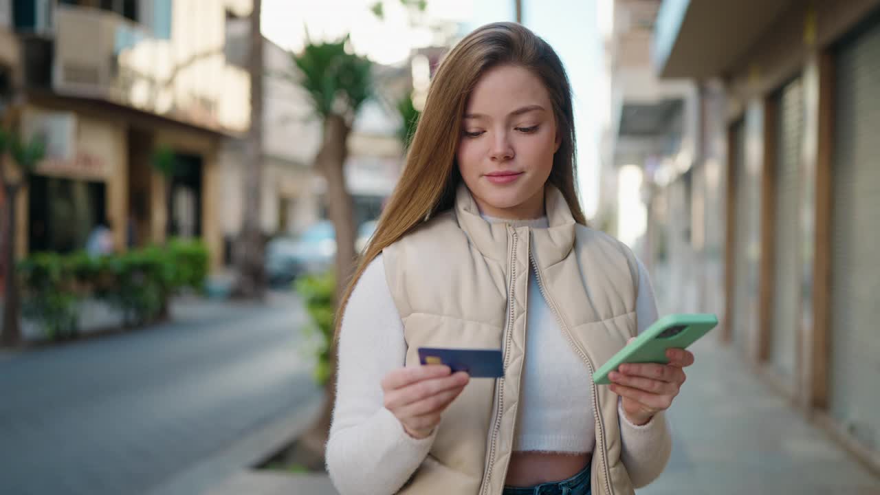 年轻的金发女人在街上用智能手机和信用卡视频素材