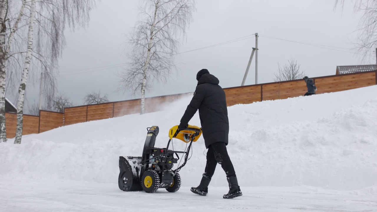 手动吹雪机的工作人员。下雪的冬天。人们用雪犁铲雪堆。孩子在背景中玩耍。慢动作视频素材