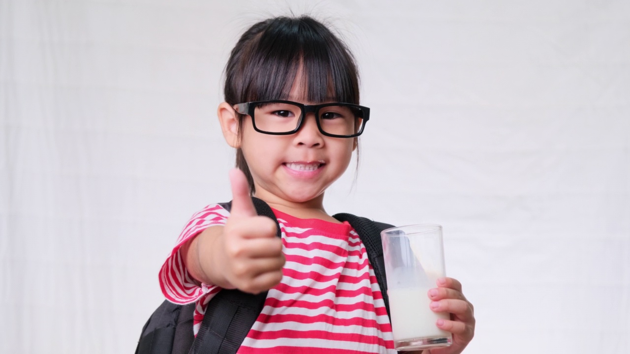 可爱的女学生在上学前用杯子喝牛奶。为儿童提供健康营养。回归学校理念视频素材