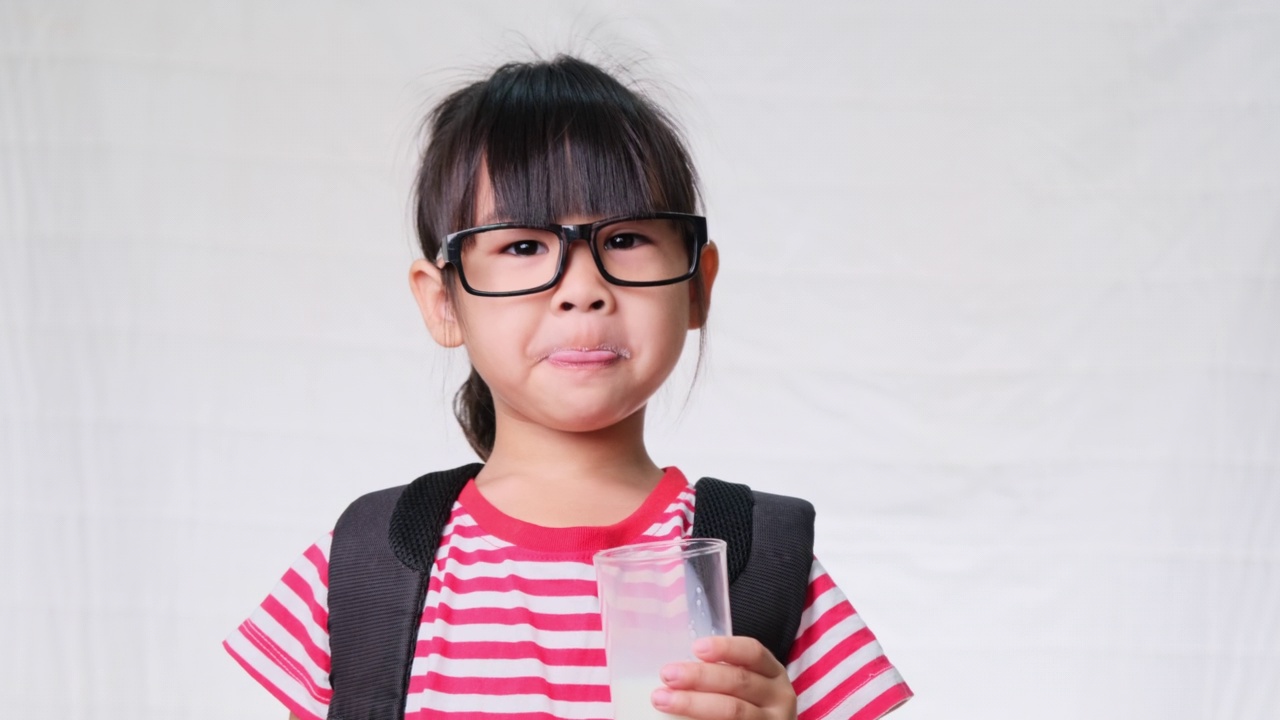 可爱的女学生在上学前用杯子喝牛奶。为儿童提供健康营养。回归学校理念视频素材