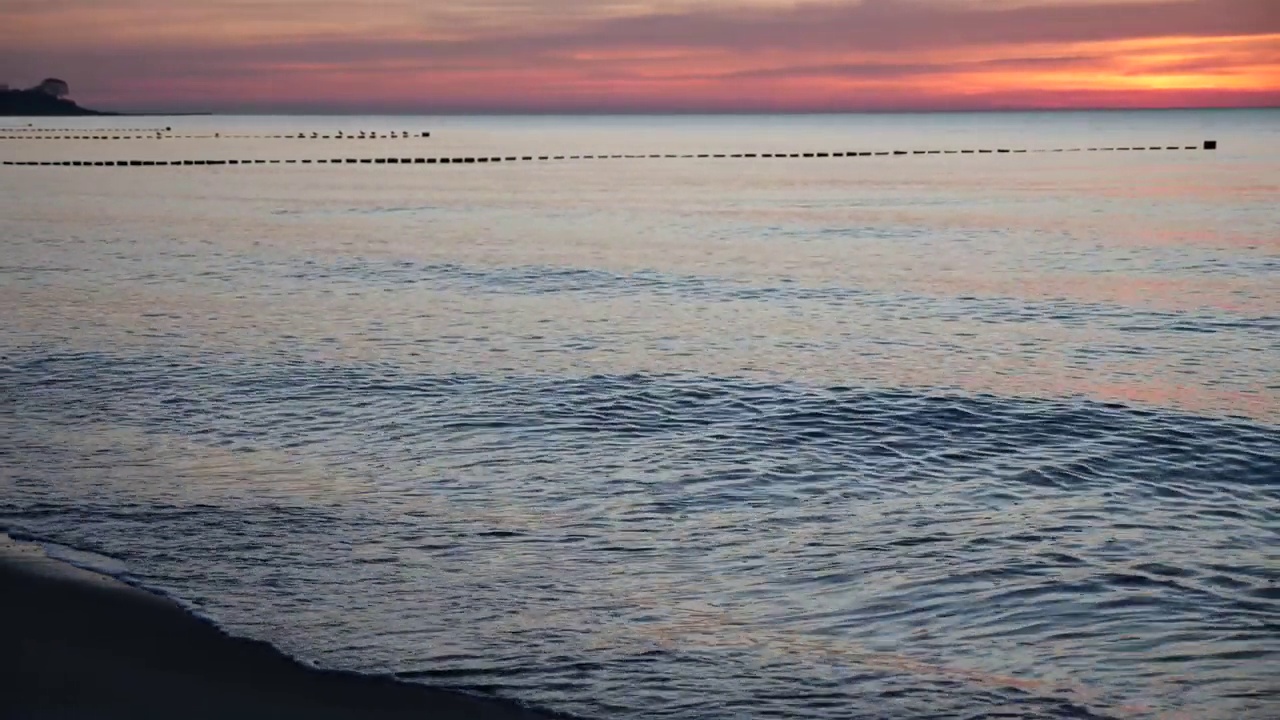 波罗的海西岸，夕阳西下，天空泛红，沙滩上的波浪视频下载