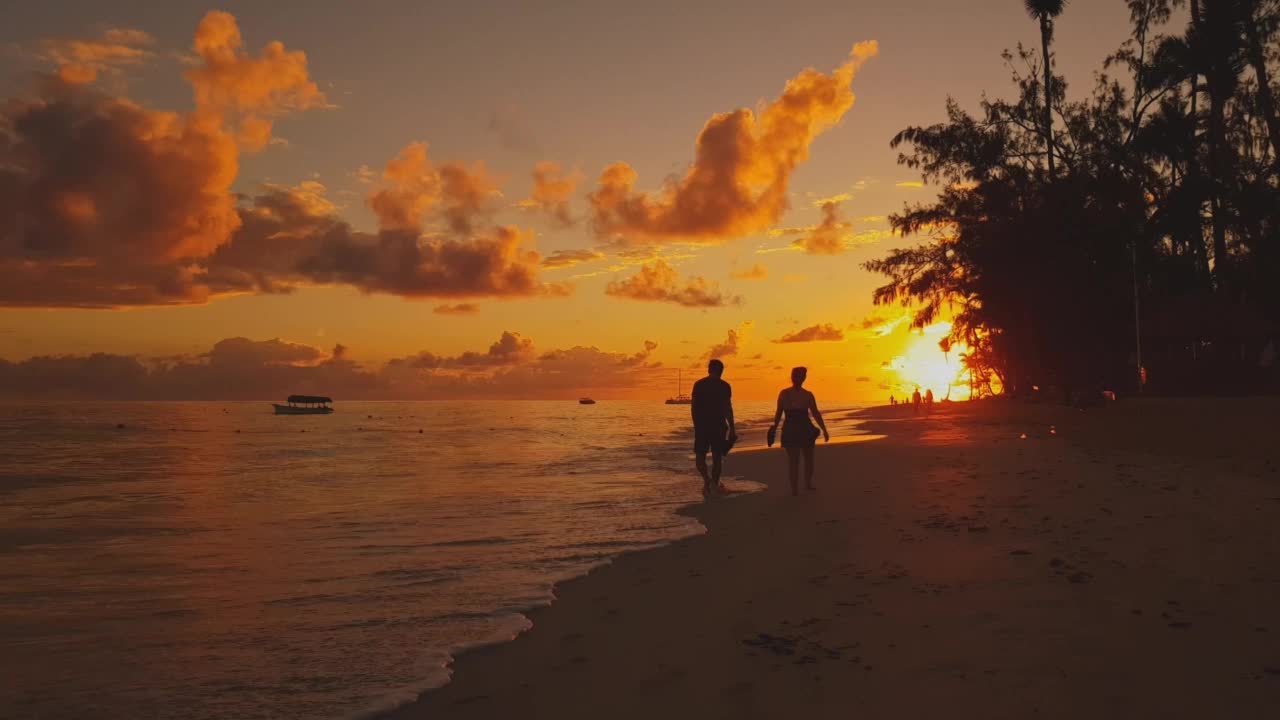 在黄金时间日落时分，人们沿着海滩上的水散步视频素材