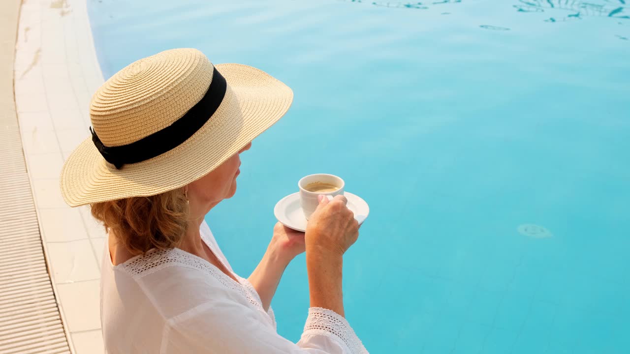 喝茶和咖啡的文化。戴草帽的女人从蓝色游泳池边的杯子里喝着热饮，奢侈的早上好，一天的开始视频素材