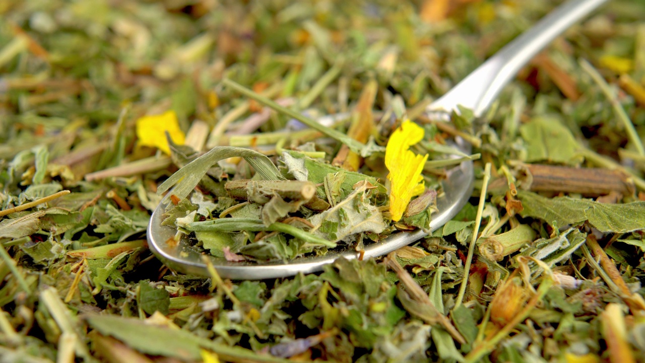 用茶匙将带有黄色花瓣的干绿茶叶子浸泡。宏。草本天然干叶视频素材