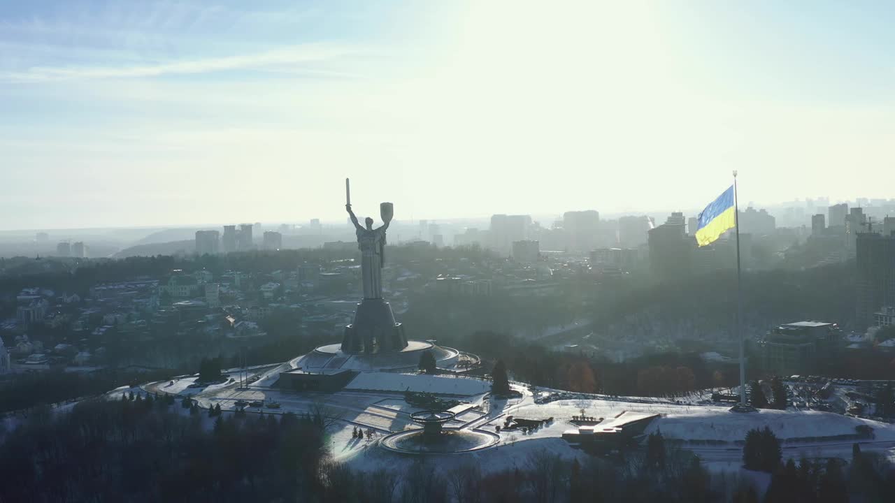 无人机升起在基辅光荣的乌克兰国旗和祖国纪念碑上，展示城市风景在阳光明媚的冬日视频素材