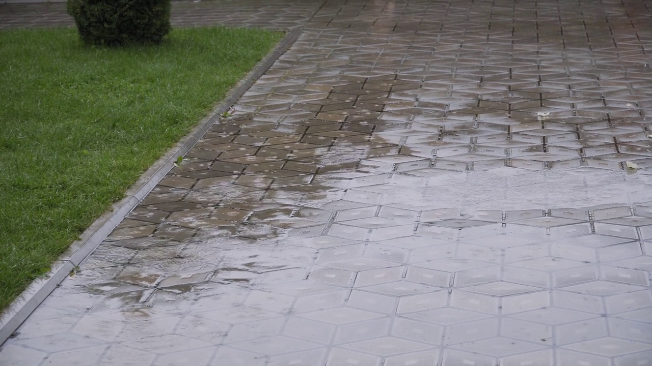 近距离观察，雨滴滴落在房子院子里的铺路板上的大水坑里。视频素材