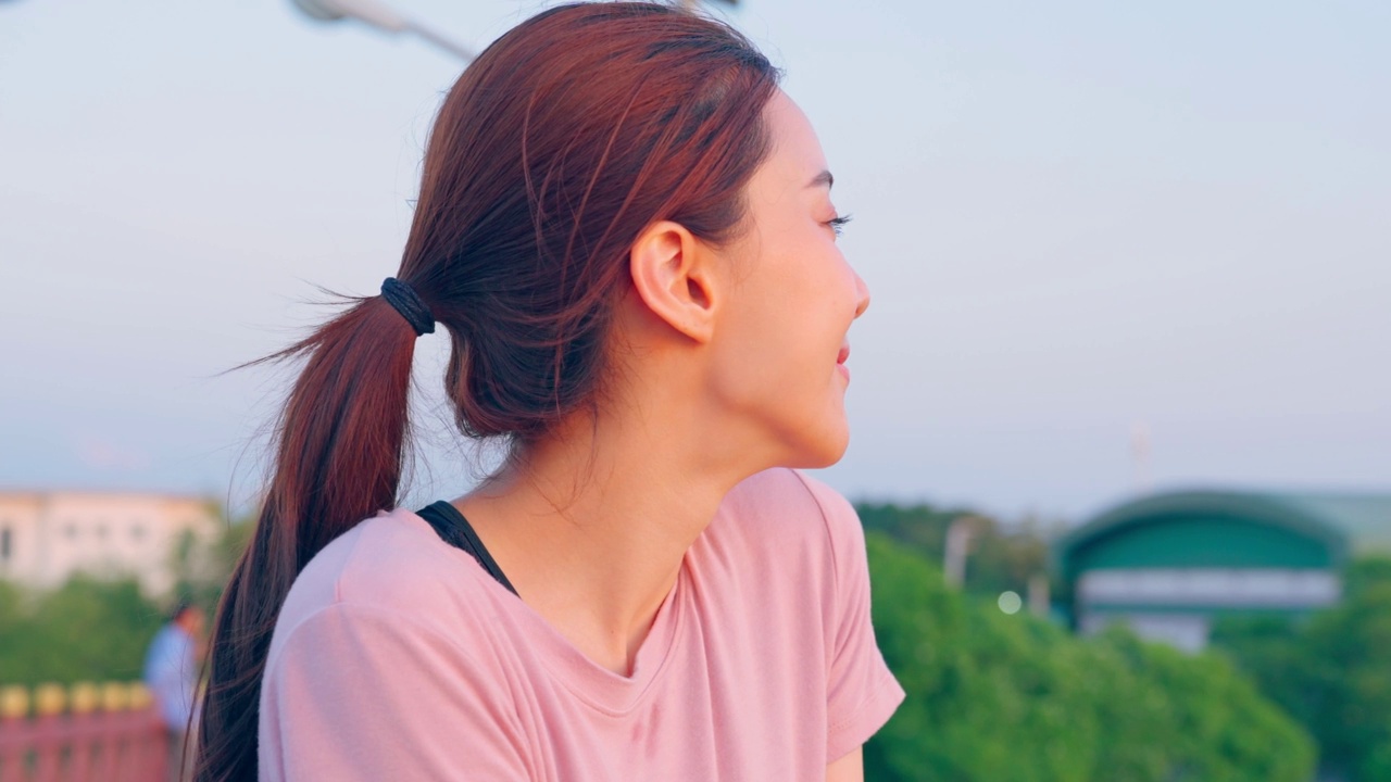 亚洲年轻的运动妇女在公园散步时深呼吸。迷人的运动员女孩穿着运动服，傍晚在花园观赏美景，运动后在户外锻炼，保健。视频素材