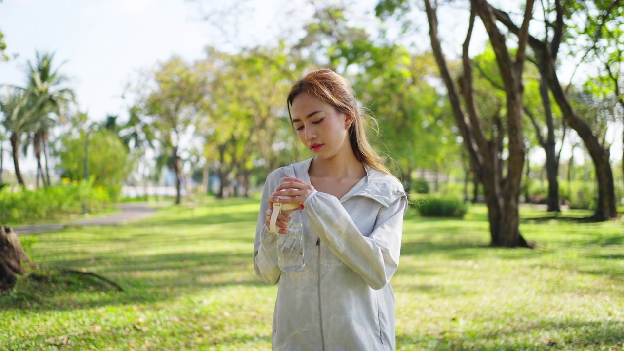 4K亚洲妇女早上在公园慢跑时喝瓶装水。视频素材