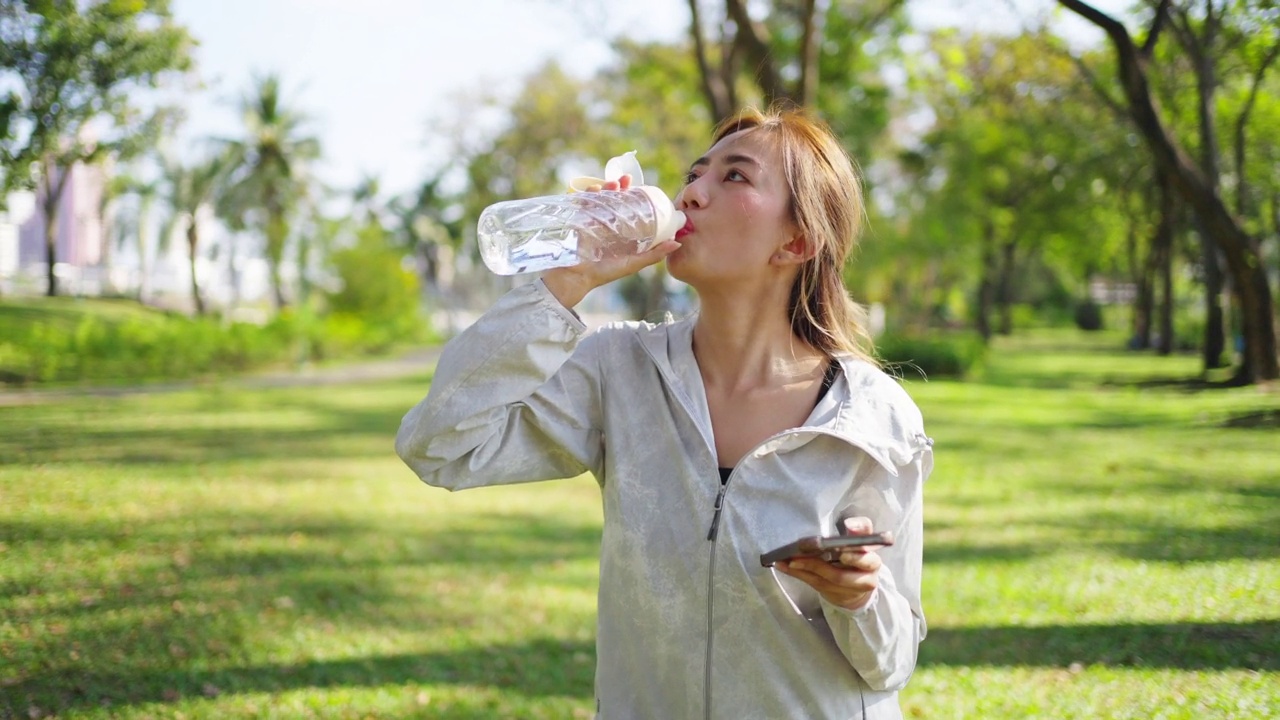 4K亚洲妇女早上在公园慢跑时喝瓶装水。视频素材