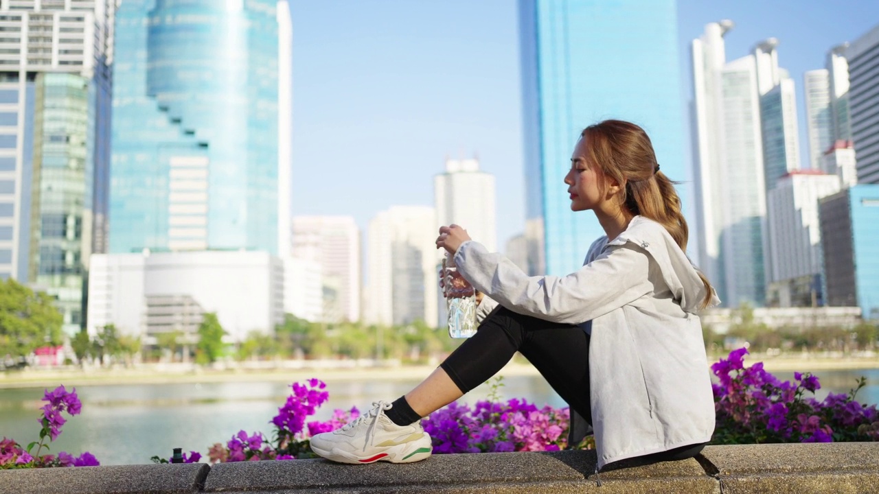 4K亚洲妇女早上在公园慢跑时喝瓶装水。视频素材